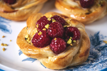 Close-up of French pastry, fresh baked puff pastry buns with raspberries and cappuccino coffee on white table, served breakfast