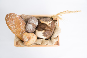 Wooden box with loafs and buns of homemade rye and wheat bread and ears. Top view. Isolated object on white background. Baking or traditional bread concept
