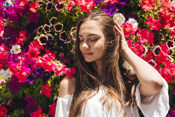 Naklejka premium covering her eyes a beautiful brunette straightens her hair against a background of blooming petunias