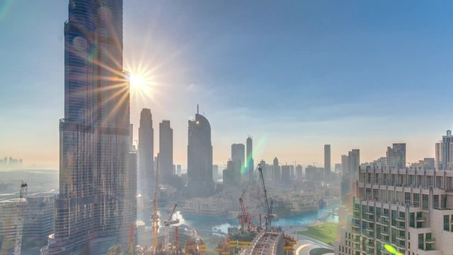 Panoramic skyline view of Dubai downtown during sunrise with mall, fountains and Burj Khalifa aerial morning timelapse. Modern skyscrapers and cloudy sky with sun rays