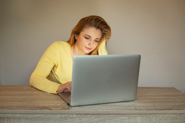 Young woman is working online. Girl with laptop. Smiling woman in  a yellow cardigan