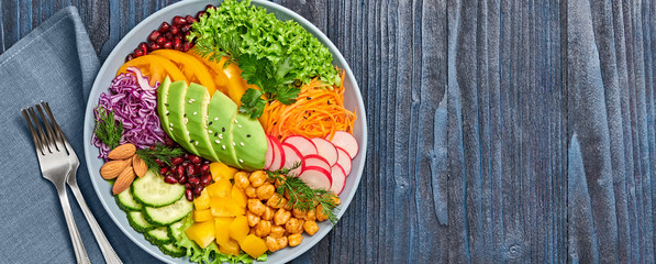 Buddha bowl salad with avocado, tomato, lettuce, cucumber, red cabbage, chickpeas, pomegranate. Vegan and balanced salad concept. Rainbow mix summer salad on wood, banner