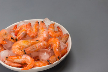 Tails of frozen shrimp and ice in white bowl.