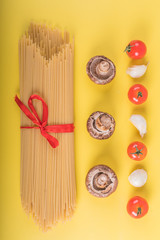 Spaghetti pasta with ingredients for cooking pasta on a yellow background. Colorful top and closeup