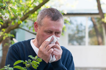 Portrait of middle aged european man blow nose on backyard background in sunny spring day