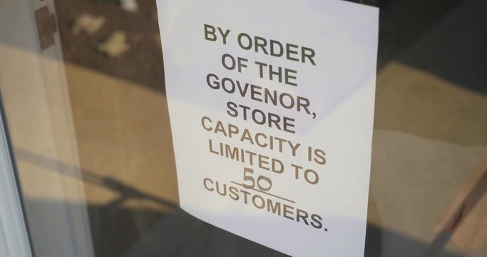 A store owner puts a COVID-19 warning sign on the front door limited customers. Reducing capacity was often required for businesses during the coronavirus pandemic of 2020.  	