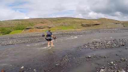 A young man crossing a frozen river on the 54 km trek from Landmannalaugar, Iceland