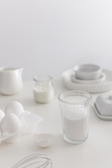 Minimal white bakery ingredients, eggs, ceramic pan, sugar, plain yogurt, whisk