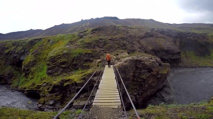 A young man with a backpack crossing a bridge on the 54 km trek from Landmannalaugar, Iceland