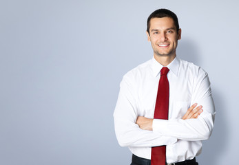 Portrait of happy smiling confident businessman, dressed in white shirt and red, crossed arms pose, with empty copy space place for some text or slogan, standing over grey background.