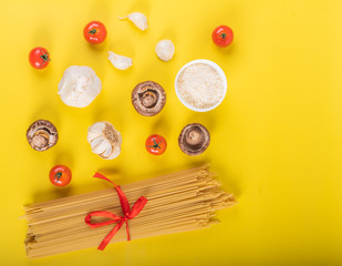Spaghetti pasta with ingredients for cooking pasta on a yellow background. Colorful top and closeup