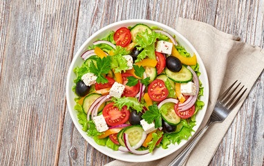 Greek salad with cucumeber, olives, feta cheese, cherry tomatoes, bell pepper and lettuce. Summer diet salad concept. Tasty greek salad in bowl on wood, top view