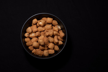 Top down image of a bowl full of granular snacks in dark copy space background. Food and product photography.