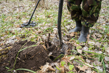 metal detector in the forest and a man digging coins. Search for precious old historical coins or metals in grass and earth. Black digger man with metal detector