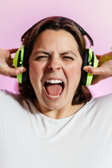 una chica caucasica de unos 40 años lleva auriculares de color verde en su cabeza.  lo tienes cogidos con la mano mientras grita y canta.
