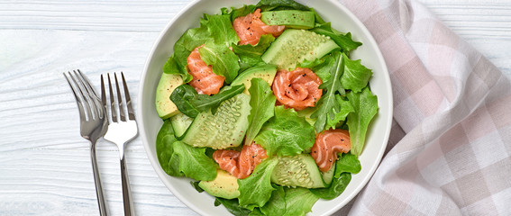 Salmon salad, cucumber, spinach, lollo, lettuce. Homemade vegetarian salmon salad. Seafood creative diet concept. Summer salmon salad on white wood, closeup, banner