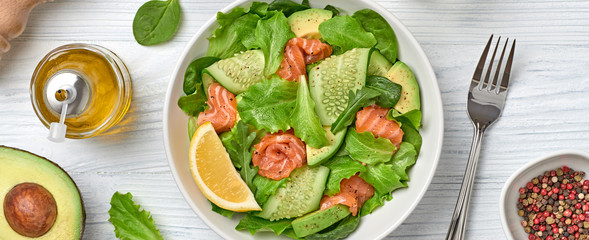 Salmon salad, cucumber, spinach, lollo, lettuce. Homemade vegetarian salmon salad. Seafood creative diet concept. Summer salmon salad on white wood, closeup, banner