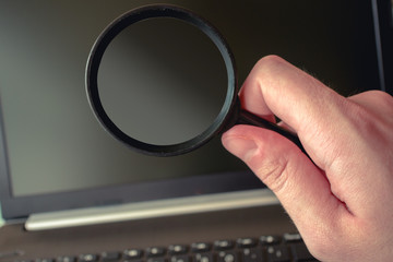 Simple photo of a magnifying glass in front of a laptop. Perfect for using it for search,...