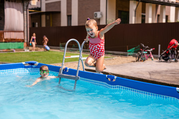 Naklejka premium Cute little girl preparing to jump into blue water, having fun in the pool, fine swimmingpool at home, summer time in daycare, holiday and vacation concept