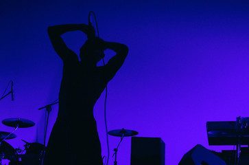 A silhouette of singer hip hop musician during live concert in blue light. Dark background, smoke,...