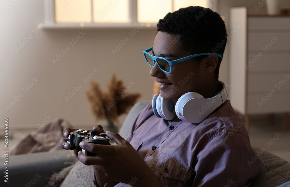 Wall mural african-american teenage boy playing video game at home in evening - Wall murals