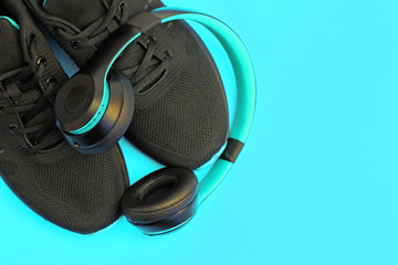 Black sneakers with headphones top view. Men's sports sneakers on a turquoise background. The concept of an active lifestyle, music, sports. Jogging in the morning. Running shoes and on-ear headphones