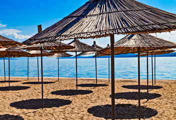 Empty beach with reed beach umbrellas, nobody on the beach. Beautiful blue sky, hot weather. Beach with no travellers and tourists. Cancellations due to coronavirus covid-19. Quarantine.