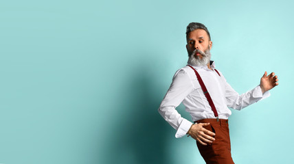 Gray-haired male in white shirt, brown pants, suspenders, black loafers. He runs looking back, posing sideways on blue background