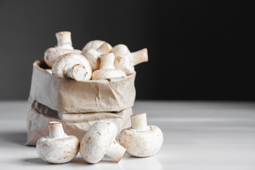Mushrooms champignons in paper bag on a white wooden table. Place for text or advertising