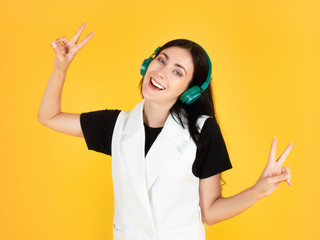 Caucasian pretty young woman raise victory hand signals about funny and positive expression while listening music song by wireless green headphone gadget device portrait isolated on yellow background