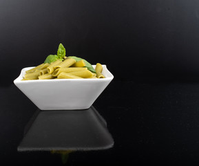Gluten-free fresh cooked penne pasta from green peas isolated on black background, basil leaf top