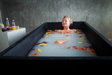 attractive slim blonde girl taking bath with milk, rose petals and citrus slices