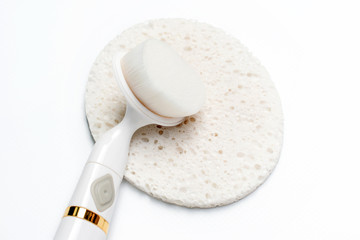 Facial brush lying on sponge. Bath accessories for face care. Facial massager and organic sponge on a light background, top view