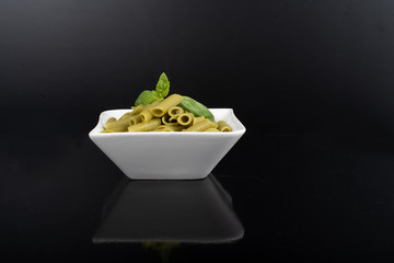 Gluten-free fresh cooked penne pasta from green peas isolated on black background, basil leaf top