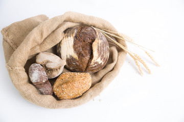 Traditional wholegrain rye buns and loafs in rustic burlap sack with ears. Top view, high angle. Isolated object on white background. Bakery or freshly baked bread concept