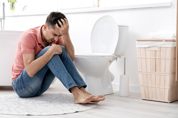 Young man suffering from anorexia near toilet bowl at home