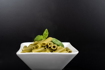 Gluten-free fresh cooked penne pasta from green peas isolated on black background, basil leaf top
