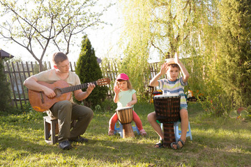 Happy family dad and two kids having fun with musical instruments together outdoors. Dad playing  guitar and kids playing ethnic drums. quarantine. musical concept