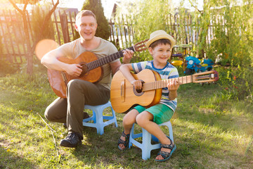 Happy family dad and child son having fun with musical instruments guitars together outdoors. Dad teaches son how to play guitar. quarantine. musical concept