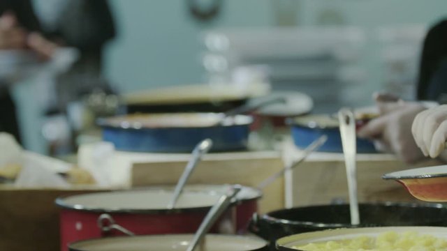  People getting food in plates in a kitchen's buffet serving line - slow motion