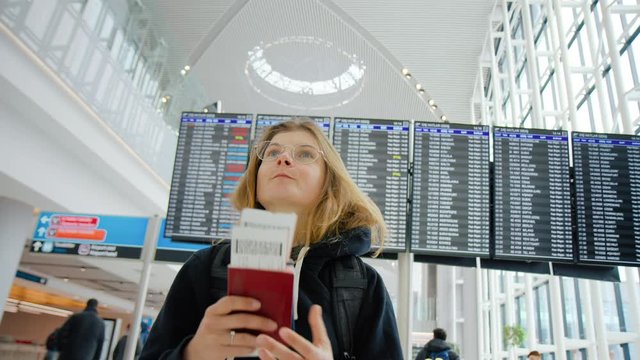 Young pretty woman with backpack wait for travel partner or couple with two flight tickets and passports. Excited for vacation or holiday. Worry not to miss flight. Airport scene, millennial traveler