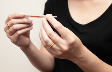 Closeup of two hands holding clinical thermometer and looking on it for checking temperature. Diagnosis and test COVID-19.