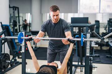 Personal trainer helping a young woman to lift a barbell while working out in a gym, Selective focus.