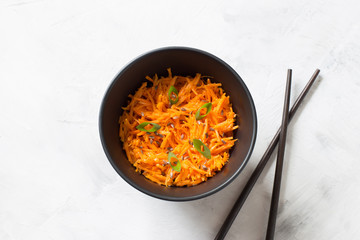 (Asian) Korean carrots-pickled, spicy salad of sliced carrots with spices and garlic in a black salad bowl on a light background close-up. A dish of Eastern vegetarian cuisine.