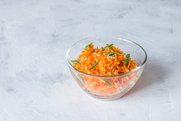 (Asian) Korean carrots-pickled, spicy salad of sliced carrots with spices and garlic in a transparent salad bowl on a light background close-up. A dish of Eastern vegetarian cuisine.
