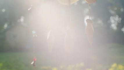 Marine wind chime made of seashells hanging outdoors backlit with sun rays lens flare. Tropical decoration spinning sunlit in summer sunlight slow motion. atmospheric wallpaper boho-chic style design