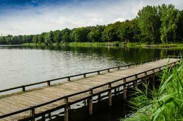 Netherlands, Zeeland region. August 2019. The beautiful pond of a campsite: the wooden pier goes into the water, in the background the forest runs alongside the shore.