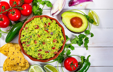 Bowl of Avocado Guacamole Mexican Dip with Avocado, Lime, Tomato, Cilantro with Fresh Ingredients on a Table with Tortilla Chips. Selective focus.