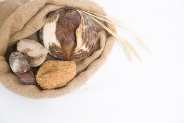 Fresh rye and wheat buns and loafs in rustic burlap sack with ears. Top view, copy space. Isolated object on white background. Bakery or homemade bread concept