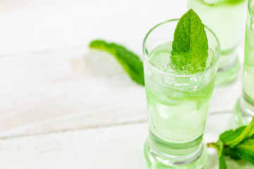 Summer Sweet Refreshing Mint Liqueur Cocktail Shots with Ice and Mint Leaves on White Wooden Background. Selective focus.